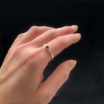 Hand wearing a silver ring with a purple gemstone on a black background