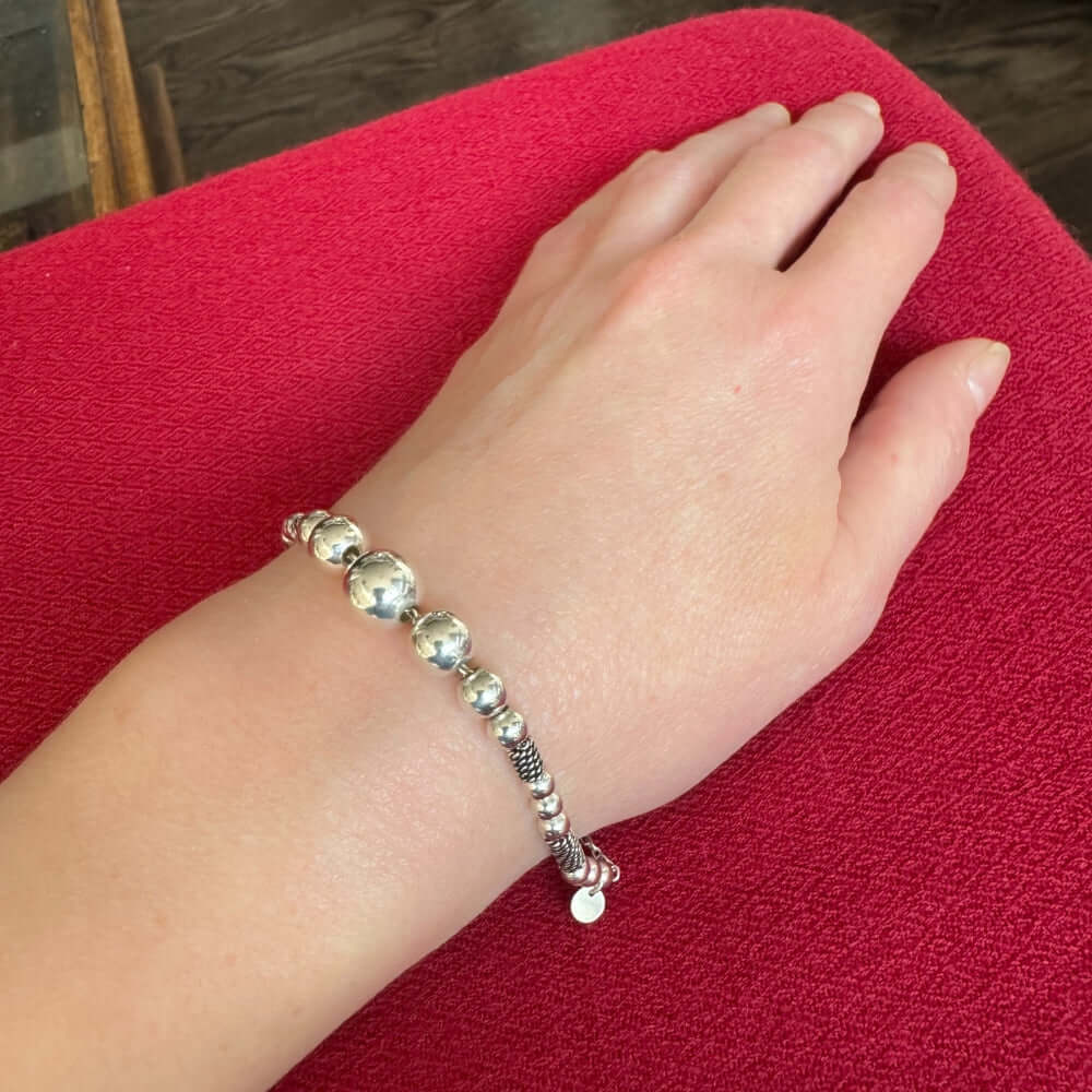Silver beaded bracelet on a wrist against a red fabric background