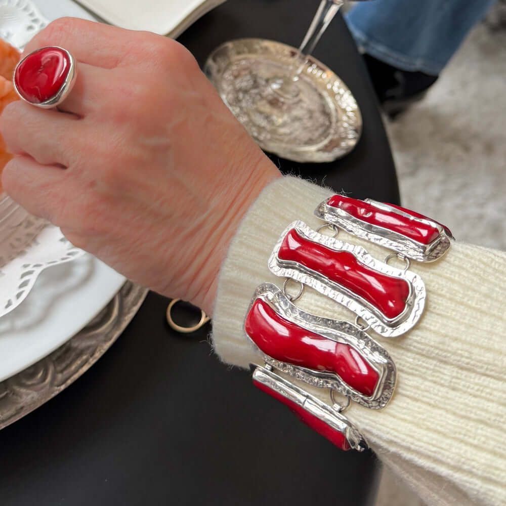 Person wearing a silver bracelet with coral, sitting at a table.