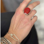 Hand wearing a red coral ring with silver band on a blurred background