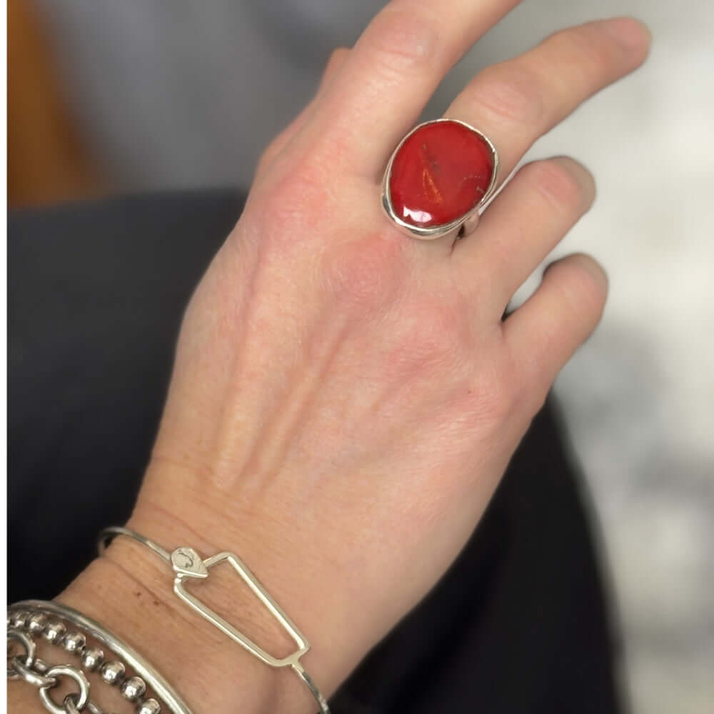 Hand wearing a red coral ring with silver band on a blurred background