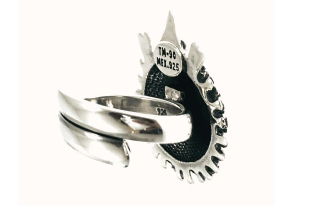 A Taxco sterling silver ring with a textured black inlay and a decorative pointed top, featuring a band with a central split design. The inside of the ring is stamped with 'TM-90 MEX.