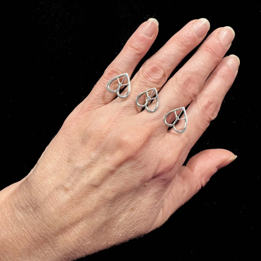 Hand wearing three silver heart-shaped ring on a black background