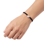 A close-up of a person's hand and wrist wearing a black braided cord bracelet with a small silver textured triangle, set against a plain white background.