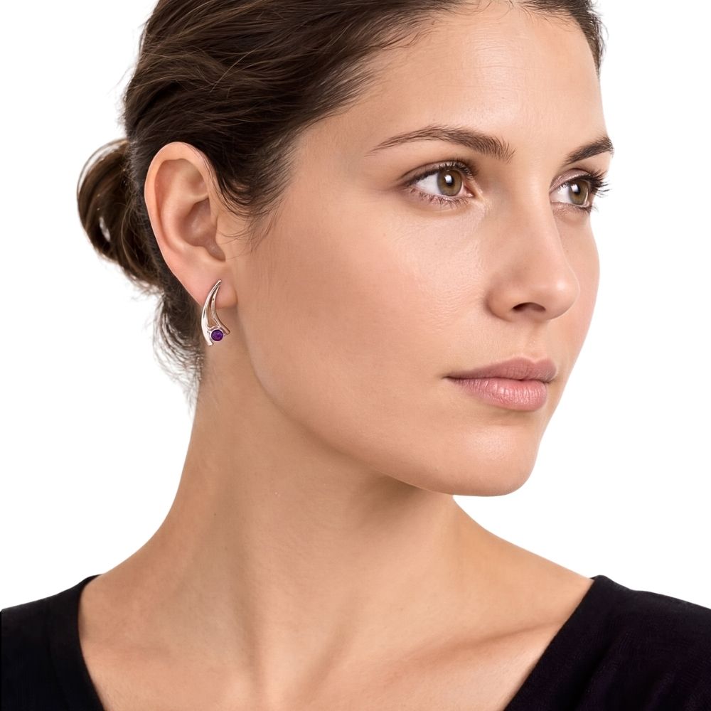 A close-up of a woman wearing a small silver crescent-shaped stud earring with a purple gemstone, shown against a plain white background.