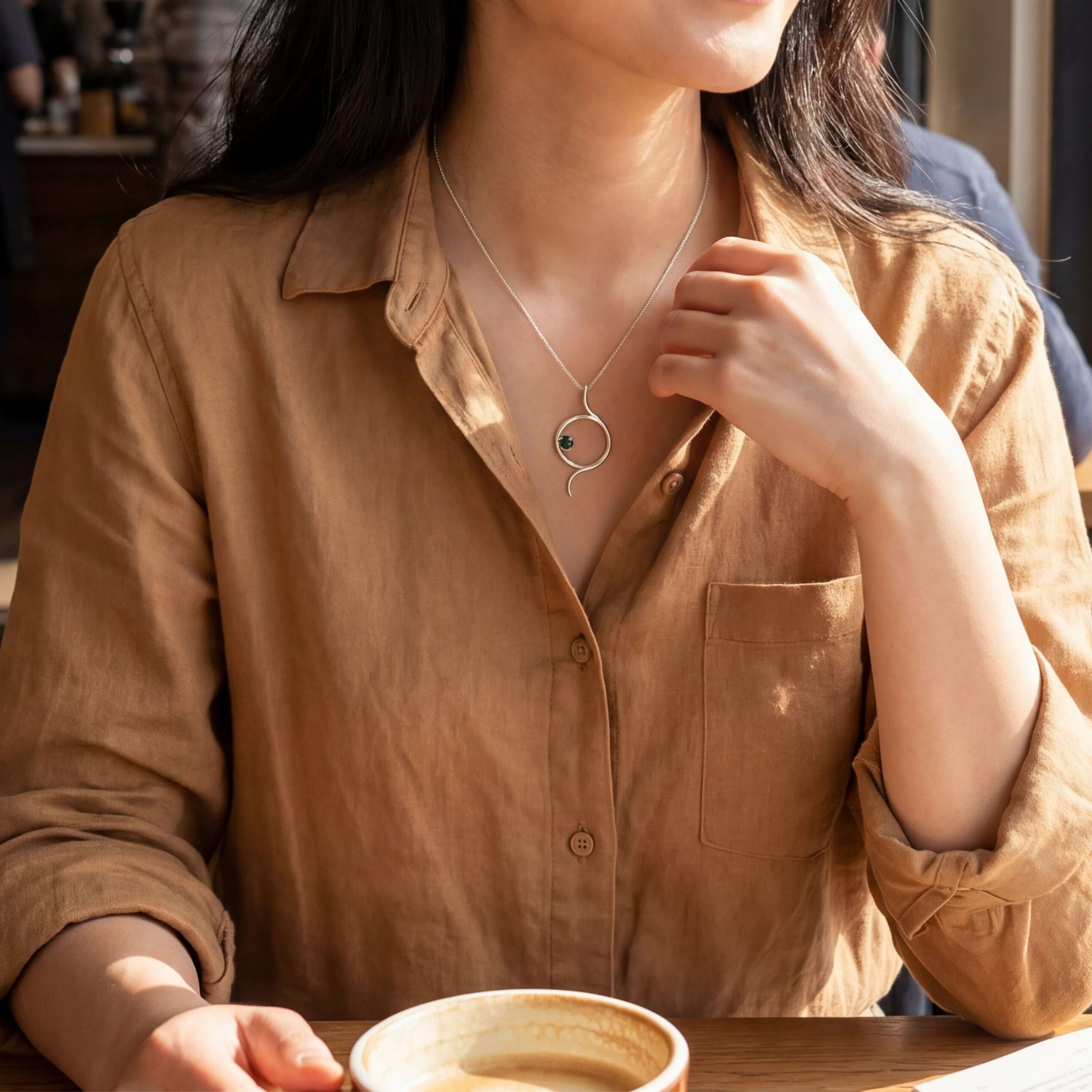 A woman in a linen shirt wearing an authentic Mexican silver artisan pendant at a cafe.