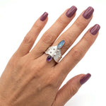 The artisan opal and amethyst ring worn on a hand, illustrating its striking scale and artistic presence.