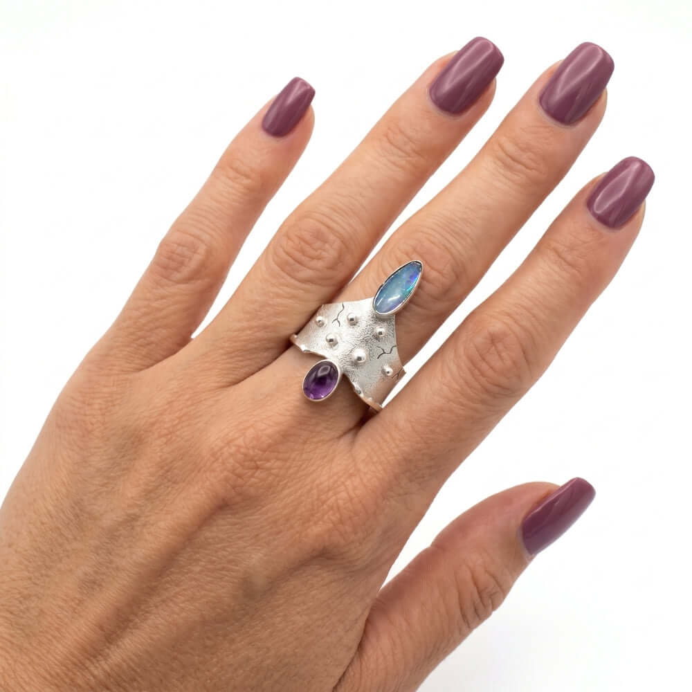 The artisan opal and amethyst ring worn on a hand, illustrating its striking scale and artistic presence.