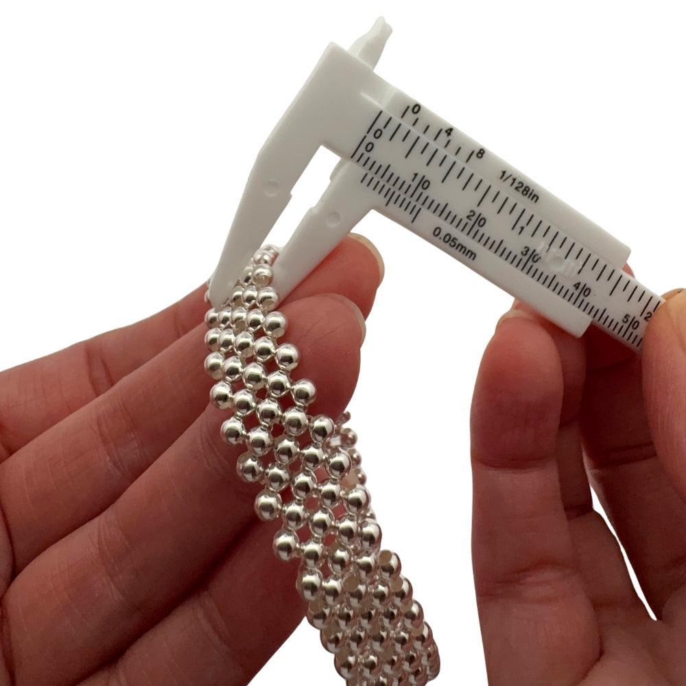 A mechanical vernier caliper measuring the size of the silver beads of the five-strand 925 silver beaded bracelet.