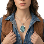 Close-up view of the artisan large oval turquoise pendant worn on a silver chain, illustrating its bold scale and rich blue tones against the skin.