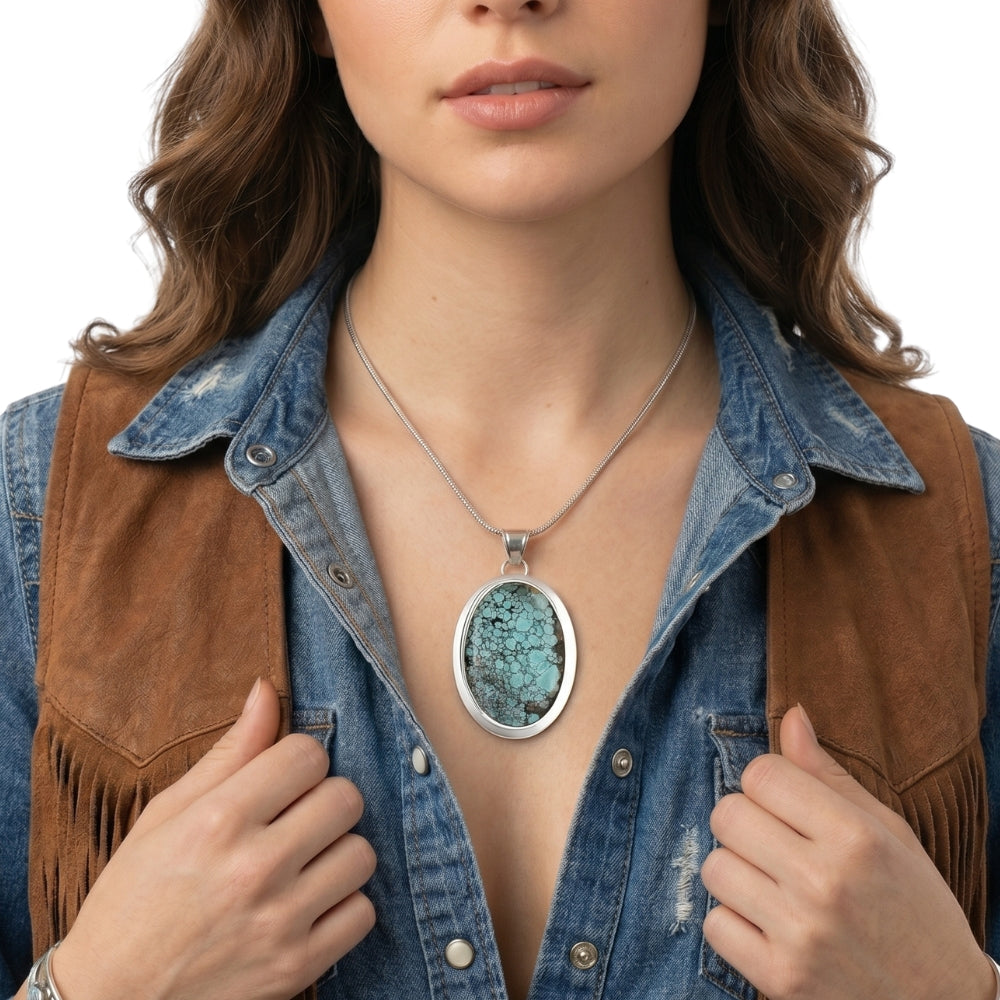 Close-up view of the artisan large oval turquoise pendant worn on a silver chain, illustrating its bold scale and rich blue tones against the skin.