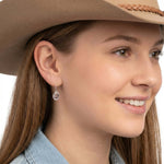 Close-up view of an artisan western silver cowboy medium hat hook earring worn on an ear.