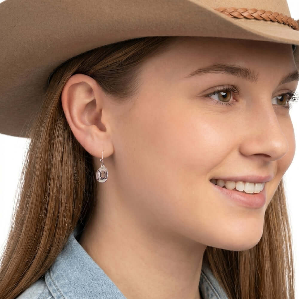 Close-up view of an artisan western silver cowboy medium hat hook earring worn on an ear.