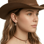 Close-up view of an artisan western silver cowboy small hat hook earring worn on an ear, illustrating its delicate daily drop scale.
