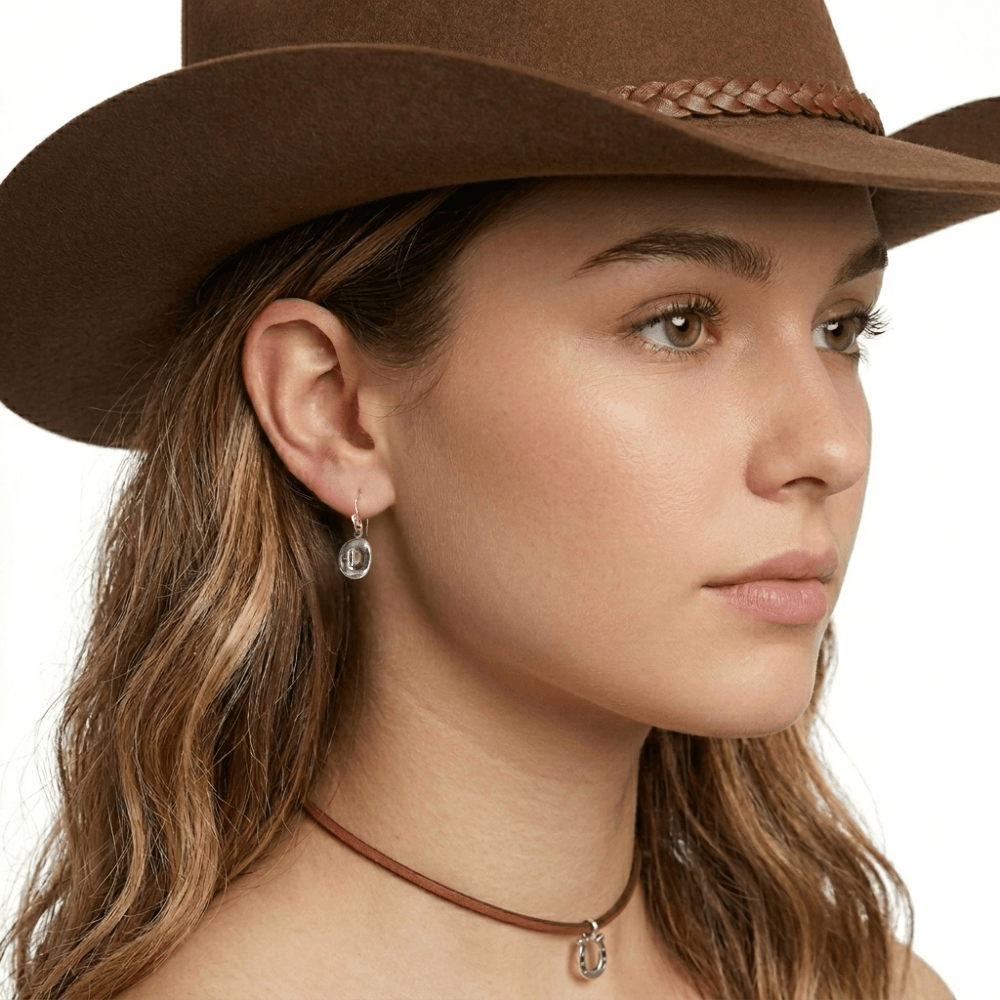 Close-up view of an artisan western silver cowboy small hat hook earring worn on an ear, illustrating its delicate daily drop scale.