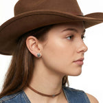 Close-up view of an artisan western silver cowboy small hat post earring worn on an earlobe, illustrating its delicate daily scale.