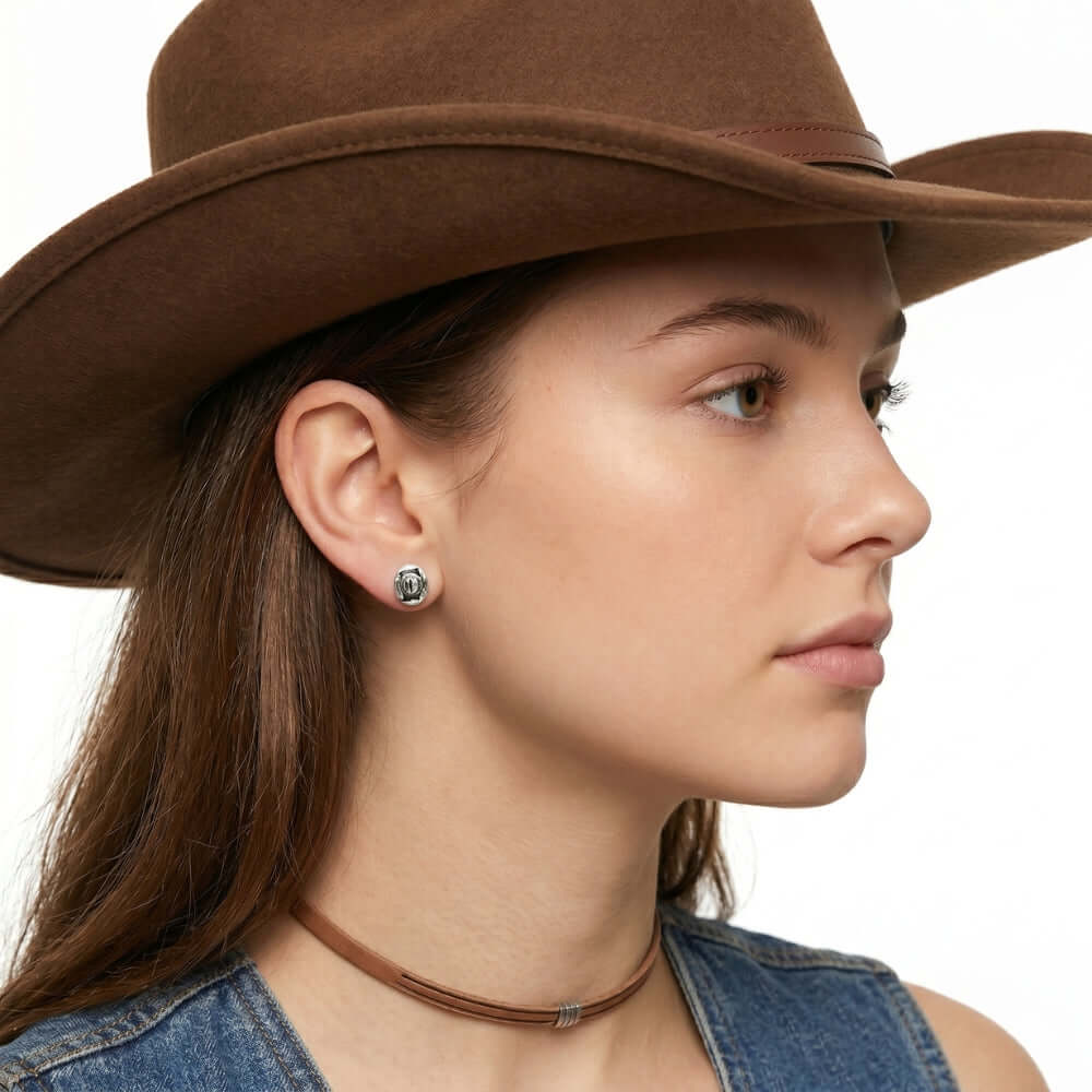 Close-up view of an artisan western silver cowboy small hat post earring worn on an earlobe, illustrating its delicate daily scale.