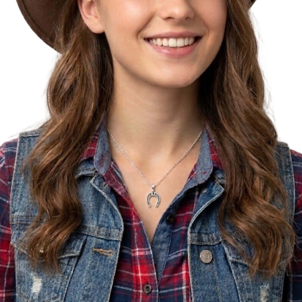 Woman wearing a denim vest over a plaid shirt with a necklace featuring a horseshoe pendant.