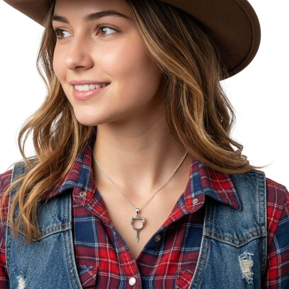 Close-up view of the artisan western silver spur pendant worn on a delicate chain against a plaid flannel shirt, illustrating its subtle daily scale.