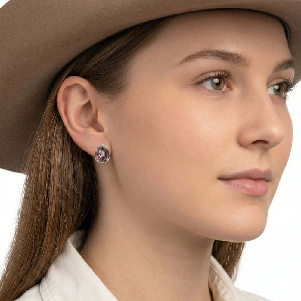 Close-up view of an artisan western silver textured hat earring worn on an ear, illustrating its delicate daily drop scale and high-contrast finish.
