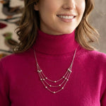 Model wearing a three-strand silver bead necklace over a pink turtleneck sweater