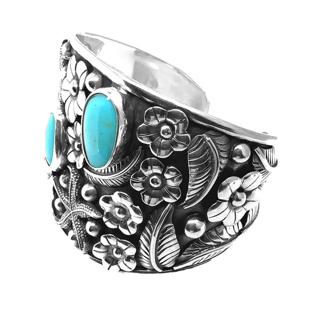 Side perspective showcasing the hand-carved botanical details, leaves, and secure bezel settings of the blue turquoise stones.
