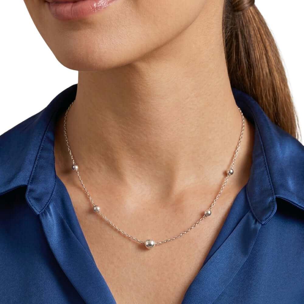 Close-up of a woman wearing a delicate Taxco silver beaded necklace with a blue shirt.