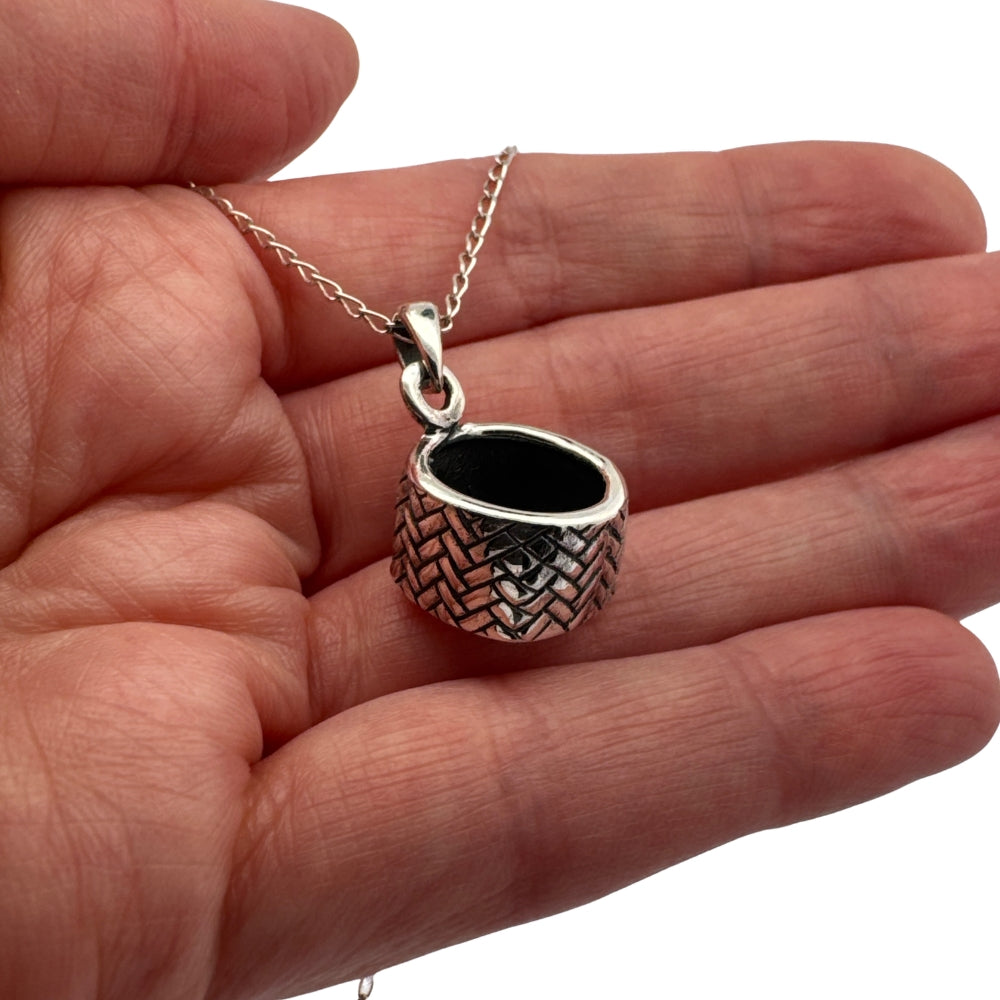 Small silver woven basket charm held in hand to show actual size