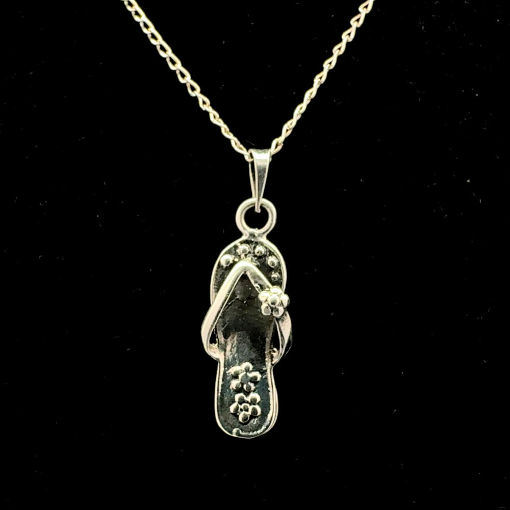 Sterling silver chancla flip-flop pendant necklace with floral detail, black background