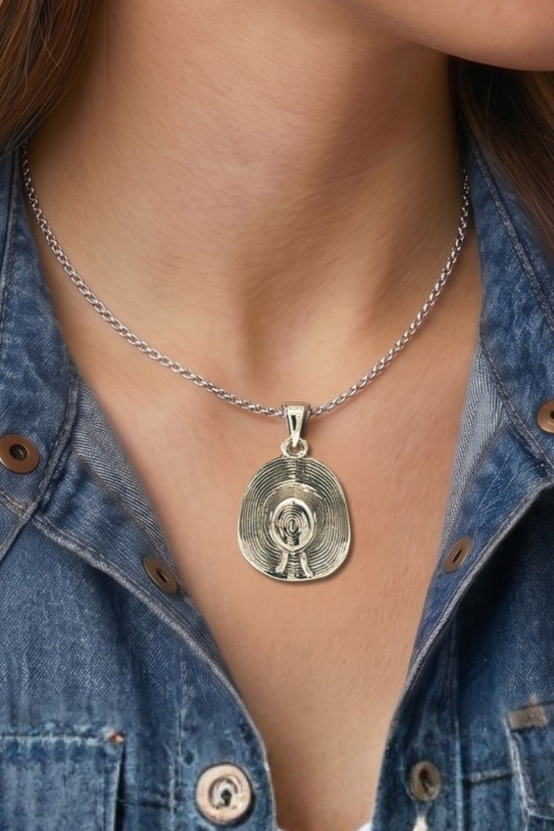 Person wearing a silver necklace with a silver cowboy hat pendant against a denim background