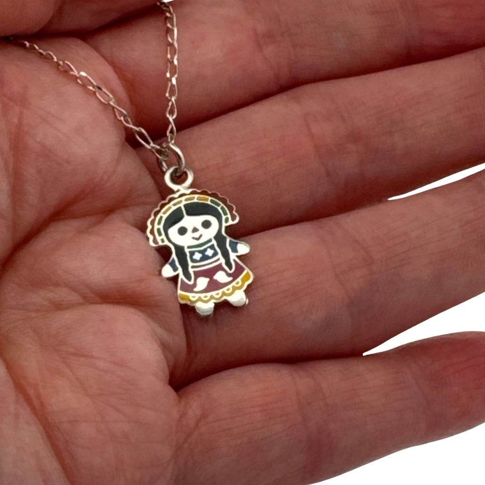 Small silver enamel Mexican Maria doll charm held in hand to show actual size
