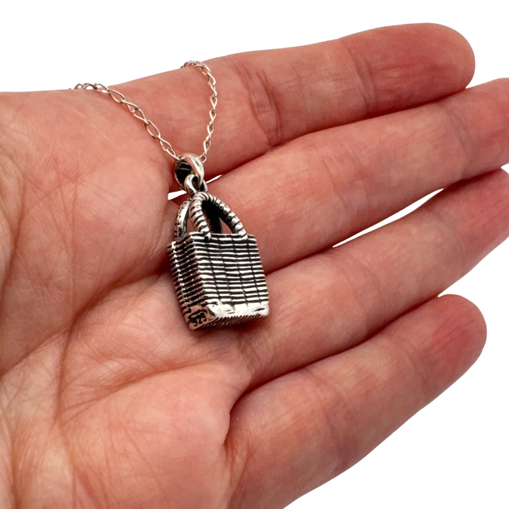 Small silver woven market bag charm held in hand to show actual size
