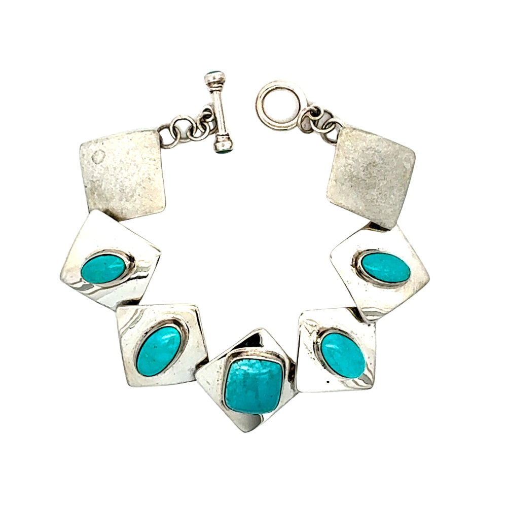 A sterling silver cuff bracelet featuring alternating square and diamond-shaped links, each inlaid with a vibrant turquoise stone, displayed on a clean white background.