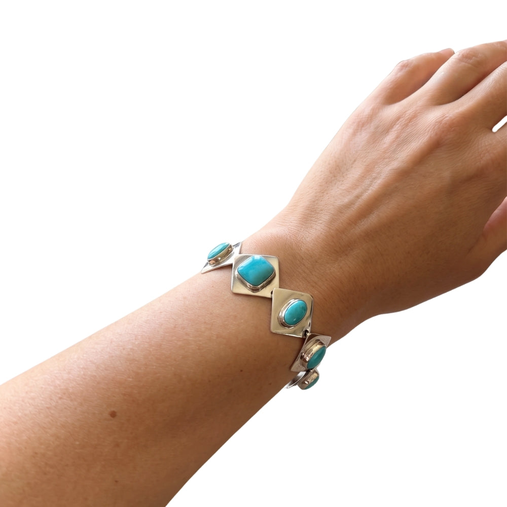 A sterling silver cuff bracelet with turquoise cabochon stones, shown worn on a person's wrist against a plain white background.