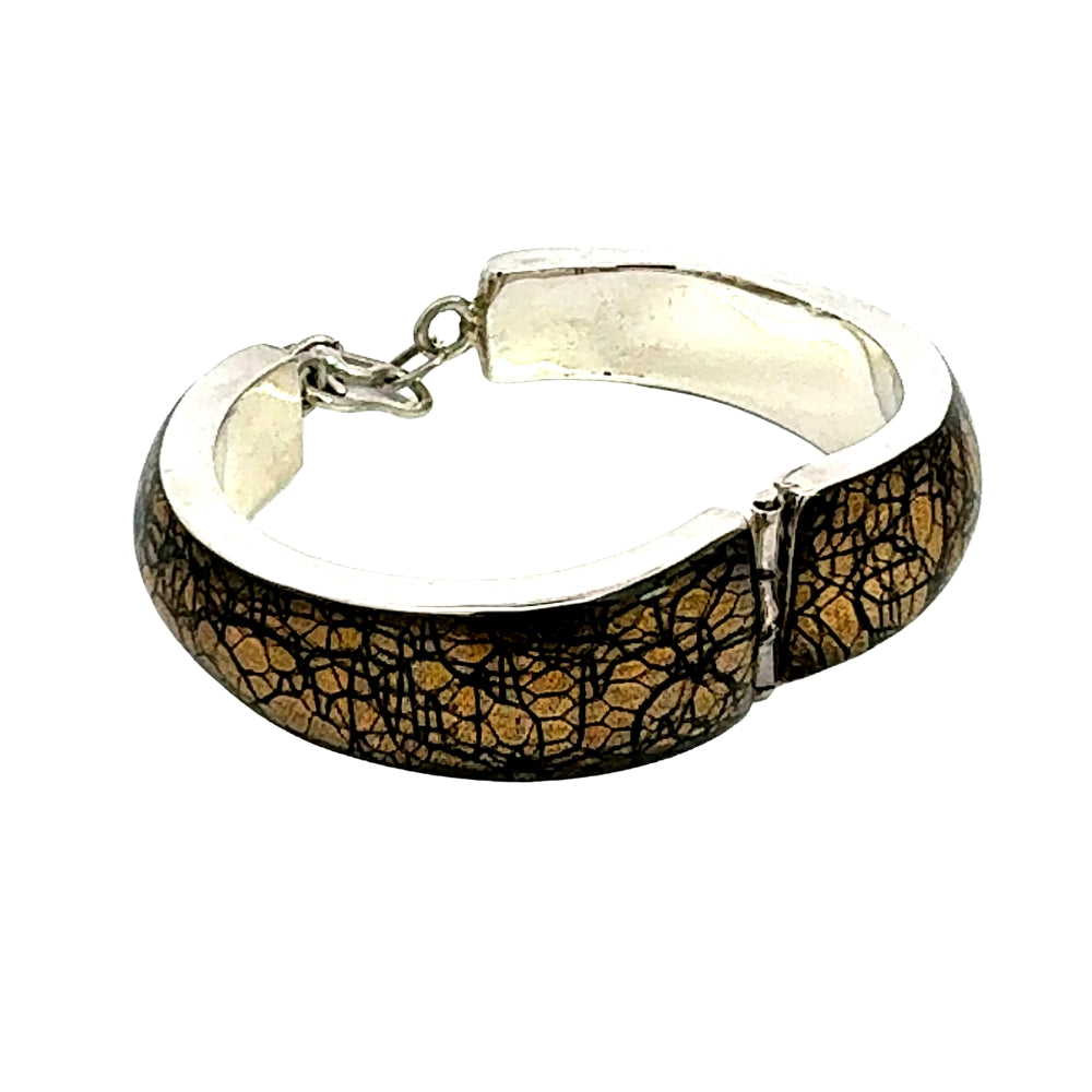 A silver-toned cuff bracelet featuring a textured, crackled gold and black pattern on the outer surface, shown against a plain white background.