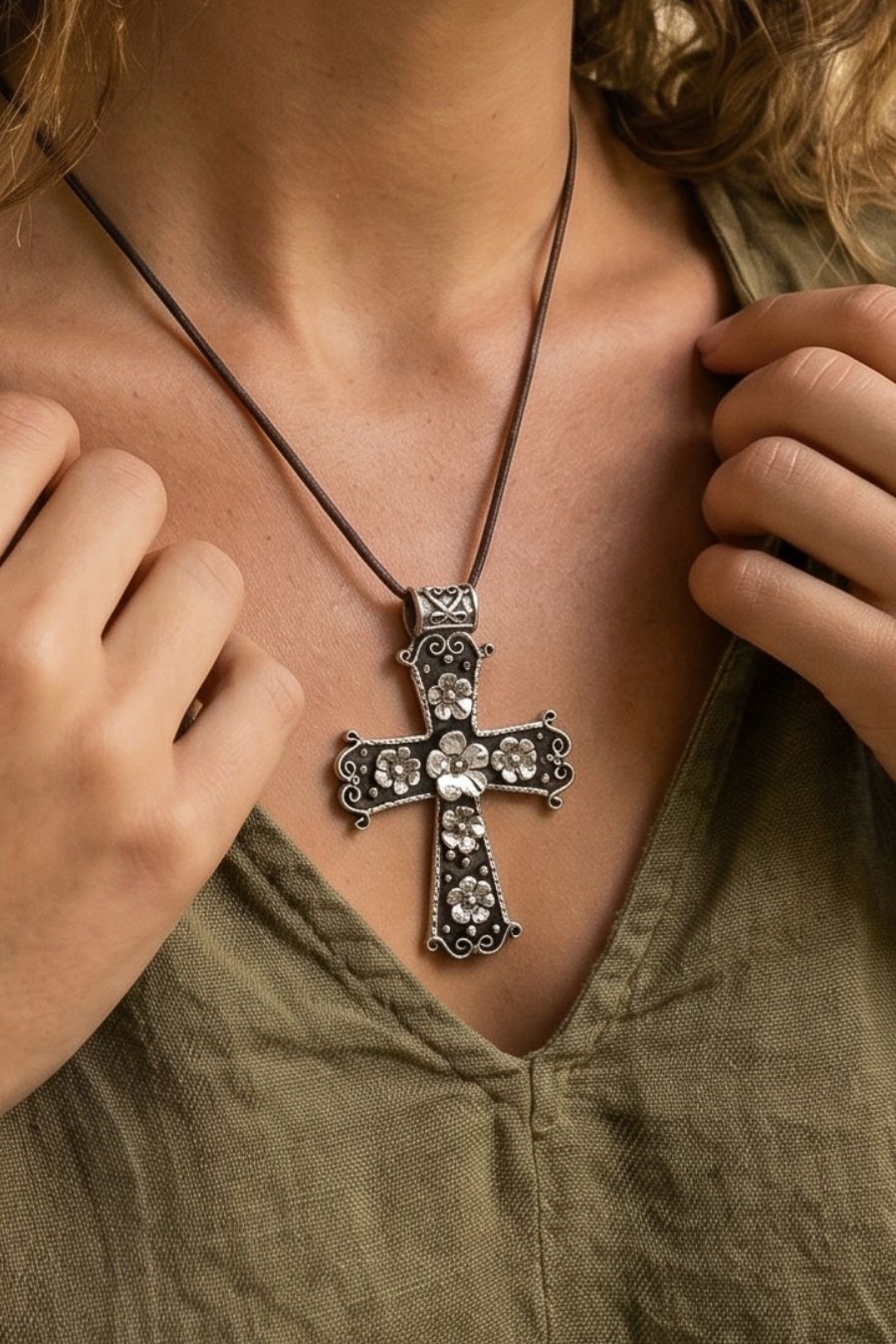 A close-up of a person wearing an oxidized Taxco silver cross pendant necklace with flowers, paired with an olive green top.