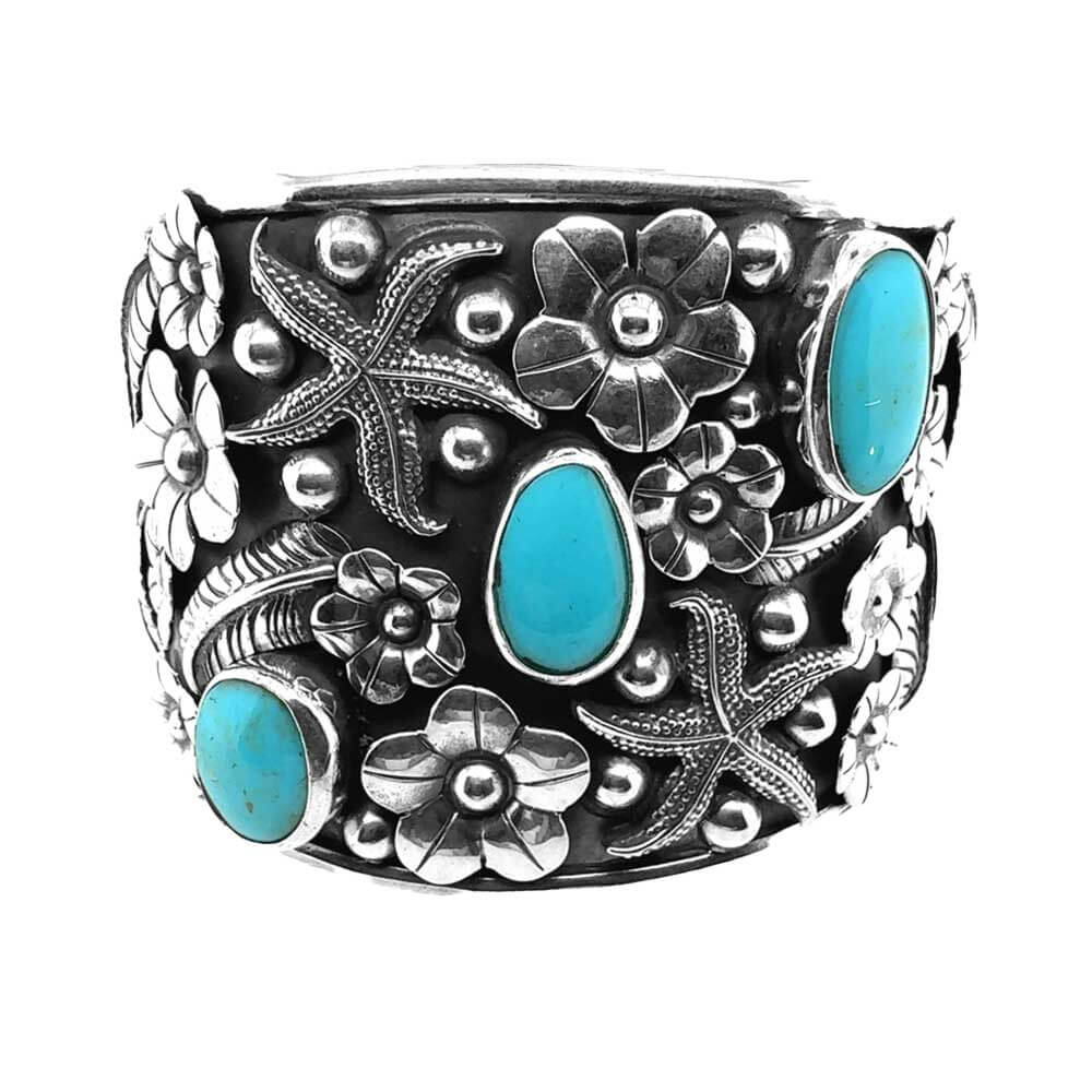 Front view of a wide handmade 925 sterling silver cuff bracelet featuring three blue turquoise stones nestled in detailed silver floral carvings.