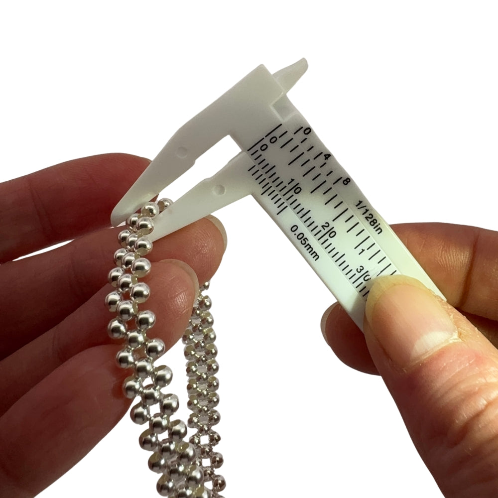 Caliper measuring the silver beads of the triple silver bracelet against a white background