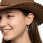 Side view of an artisan silver cowboy boot drop earring worn with a western hat, illustrating its delicate scale and elegant dangle.
